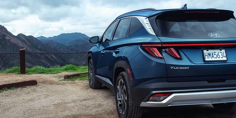 Blue Hyundai Tucson SUV parked at a mountain overlook with rugged hills in the background